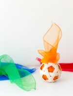Pelota Pikler con un pañuelo naranja en su interior. Alrededor hay otros pañuelos de color rojo, verde y azul