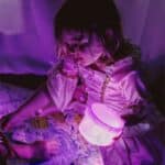 Niña sujetando una caja transparente con los Cubos sensoriales de luz GloPals lilas dentro encendidos
