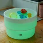 Mesa de experimentación con agua, arena y luz led encendida en color verde, rellena de agua y con jarras para trasvases.