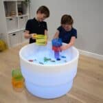 Niños jugando con la mesa de experimentación con agua, arena y luz led encendida en color blanco.