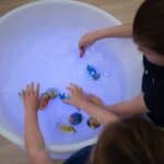 Niños jugando con la mesa de experimentación con agua, arena y luz led encendida en color blanco.