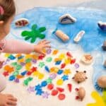 Niña jugando con las conchas translúcidas de colores en un minimundo marino.