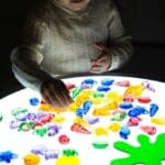 Niña jugando con las conchas translúcidas de colores en la mesa de luz.