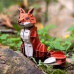 Mini puzzle 3D móvil de un zorro rojo apoyado en la tierra al lado de un árbol.
