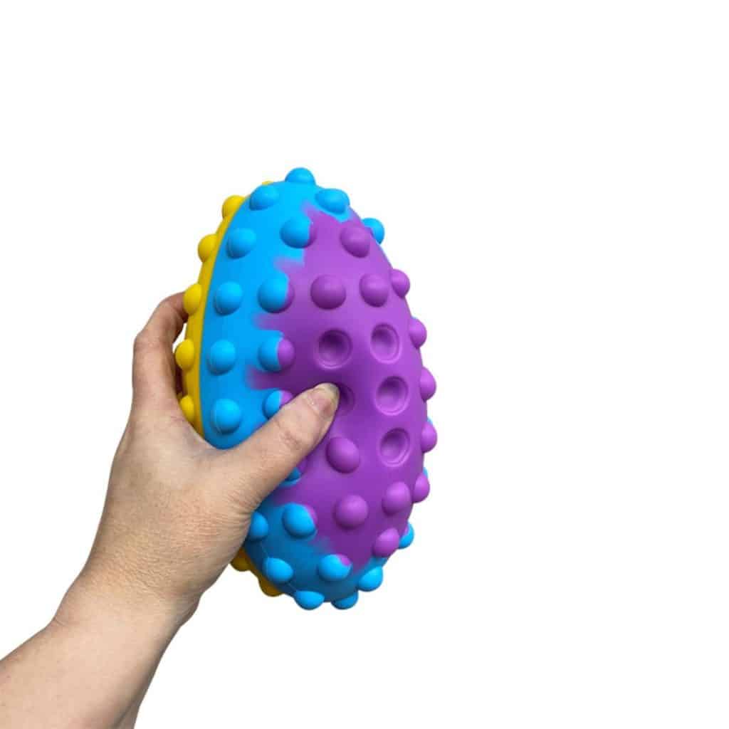Mano sujetando la pelota sensorial de rubgy pop it