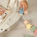Niña jugando con las piezas para ensartar incluidas en la Caja Juega y aprende 18-24 meses, set de 4 juguetes