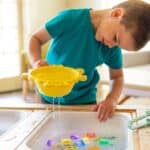 Niño jugando con el cubo tamizador del pack de Herramientas sensoriales Pick up Pals
