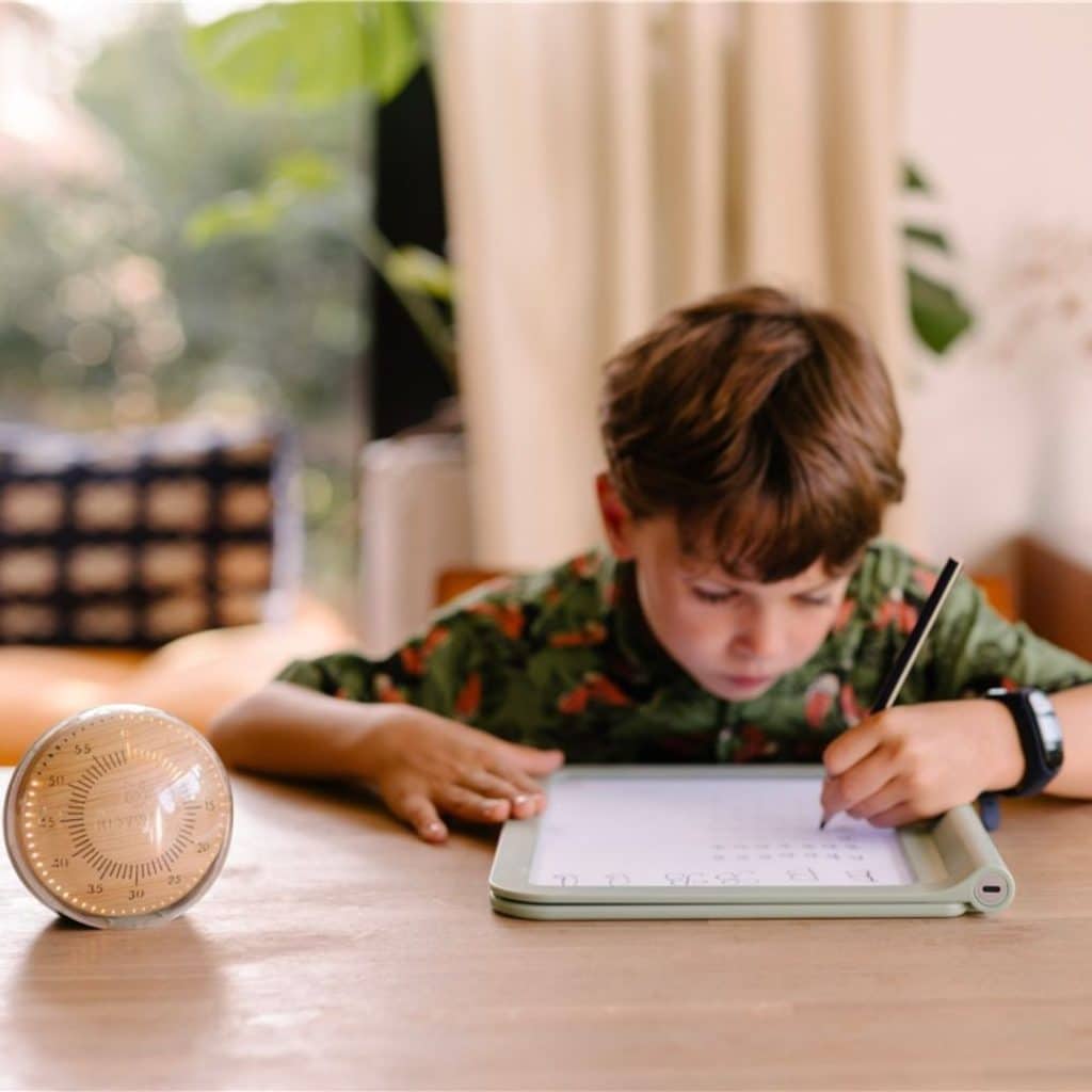 Niño escribiendo en una hoja con el Kidytimer al lado