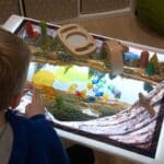 Niño jugando con el Vinilo A2 para minimundos temática lago sobre una mesa de luz