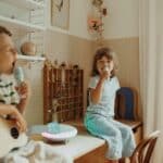 Niña y niño sentados en una mesa cantando con el Altavoz karaoke portátil con dos micrófonos Kidykaraoke