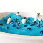 Mesa de juego sensorial con pinguinos, osos y gemas sobre una base sensorial viscosa y moldeable de gelatina azul