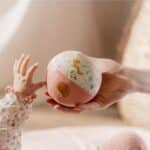 Mano de persona adulta ofreciéndole la Pelota mini blandita Fairy Garden de Little Dutch a la mano de un bebé