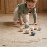 Niño sentado en una alfombra jugando con las Rocas de madera para apilar Forest Friends de Little Dutch