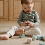 Niño sentado en una alfombra jugando con las Rocas de madera para apilar Forest Friends de Little Dutch