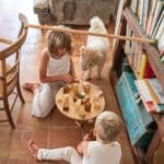 Niña y niño jugando en un salón con la Tabla de equilibrio y piezas de madera El péndulo de Grapat