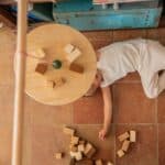 Niño tumbado debajo de la Tabla de equilibrio y piezas de madera El péndulo de Grapat