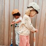 imagen de una niña con su patinete con el imagen de portada del Casco melocotón de Liewood XS/44-48CM