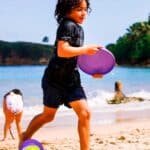 imagen de una niña jugando en la playa con el frisbee moradp