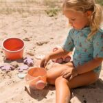 imagen de una niña jugando con la regadera del Set de juguetes de playa cubo naranja de Monnëka