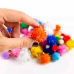 Imagen de una mano con 100 pompones con brillo para manualidades