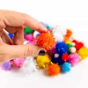 Imagen de una mano con 100 pompones con brillo para manualidades
