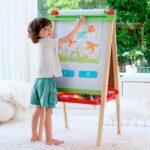 imagen de una niña con la Pizarra caballete de pintura regulable en altura de Hape