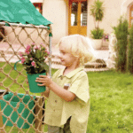 imagen de una niña con flores en las macetas incluidas en la Cabaña con arenero de madera Sandbox de Hape