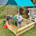 imagen de una niña experimentando con la Cabaña con arenero de madera Sandbox de Hape