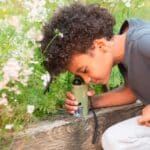 imagen de un niño con el Microscopio de bolsillo con luz led de Kikkerland, el accesorio perfecto para nuestras aventuras al aire libre.