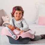 imagen de una niña jugando con el Maxi Cosi para muñecos con asa de transporte