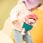 imagen de un niña con la Muñeca blandita Jeanne con mochila portabebés de Janod