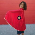 imagen de una niña con la Capa disfraz de Superhéroe reversible talla 5/6 de Great Pretenders por la parte roja