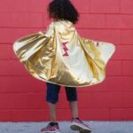 imagen de una niña con la Capa disfraz de Superhéroe reversible talla 5/6 de Great Pretenders por la parte dorada
