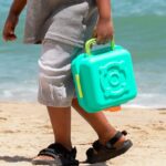 imagen de un niño trasportando con el asa la Cocina de playa portátil de Hape con accesorios