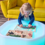 imagen de una niña con el Puzzle encajable de madera Animales de la Selva de Tickit sobre una mesa de luz